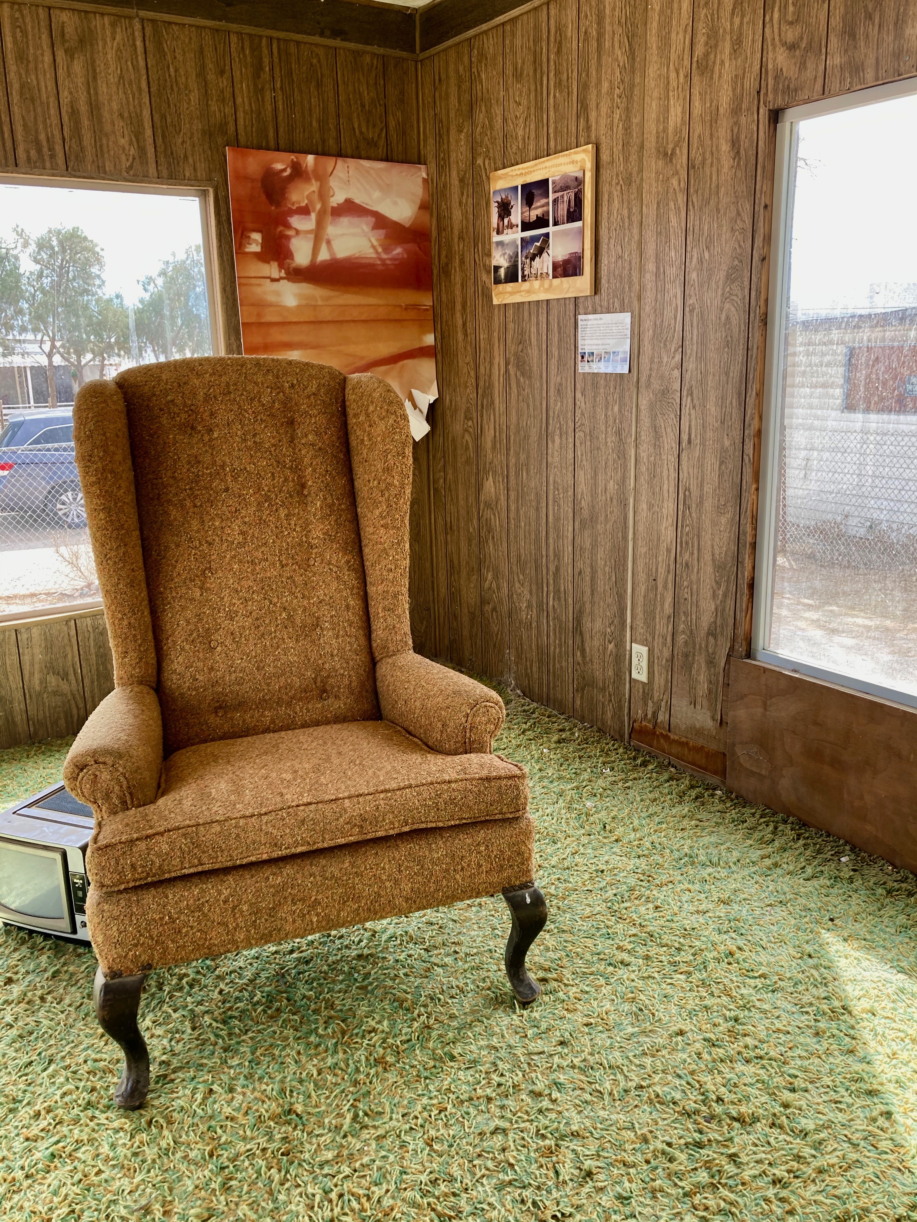 domestic interior of old trailer with armchair, shag rug, and photographs on wood panelled walls 