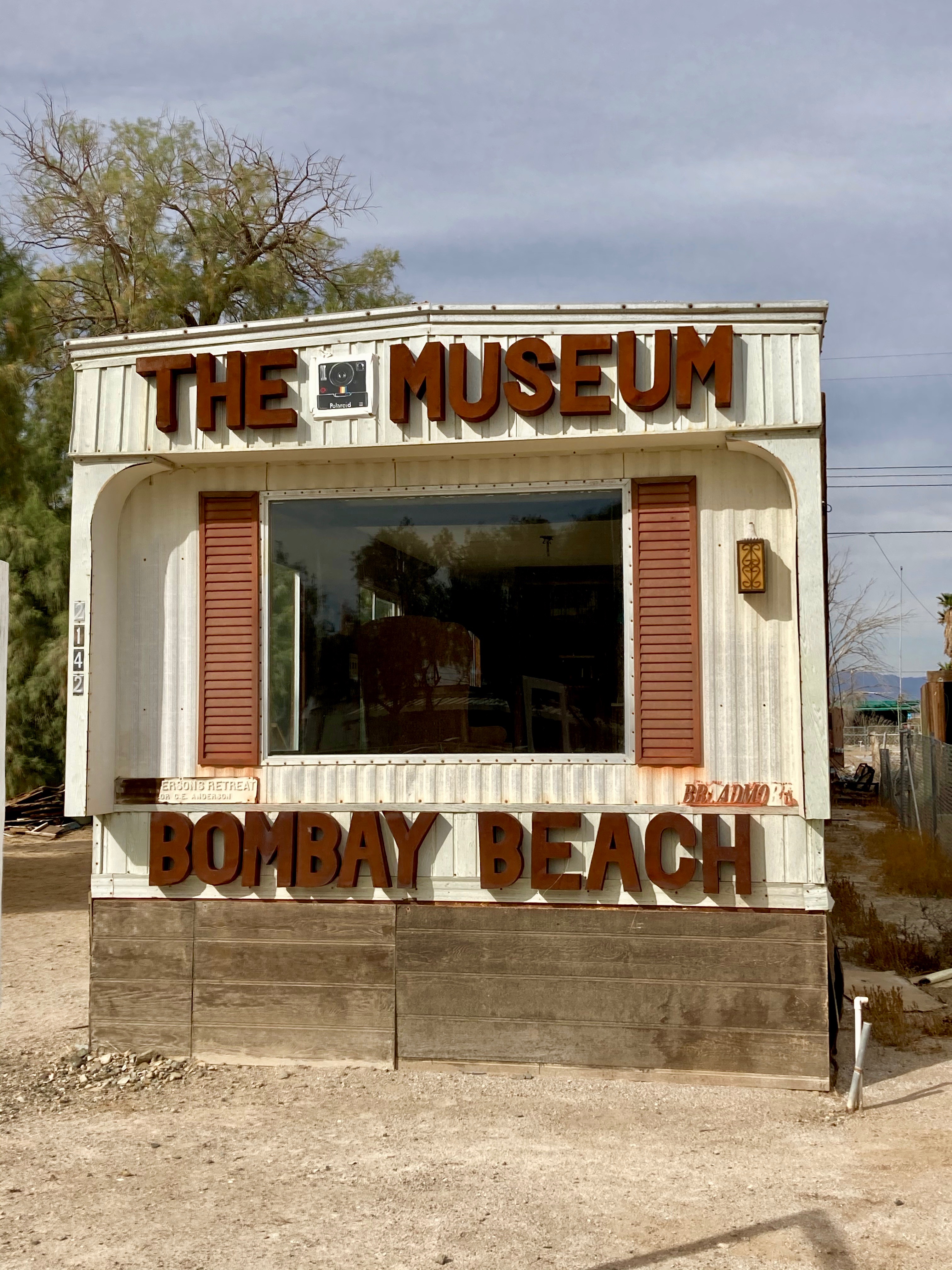 exterior view of a white trailer labeled Museum Bombay Beach in large letters